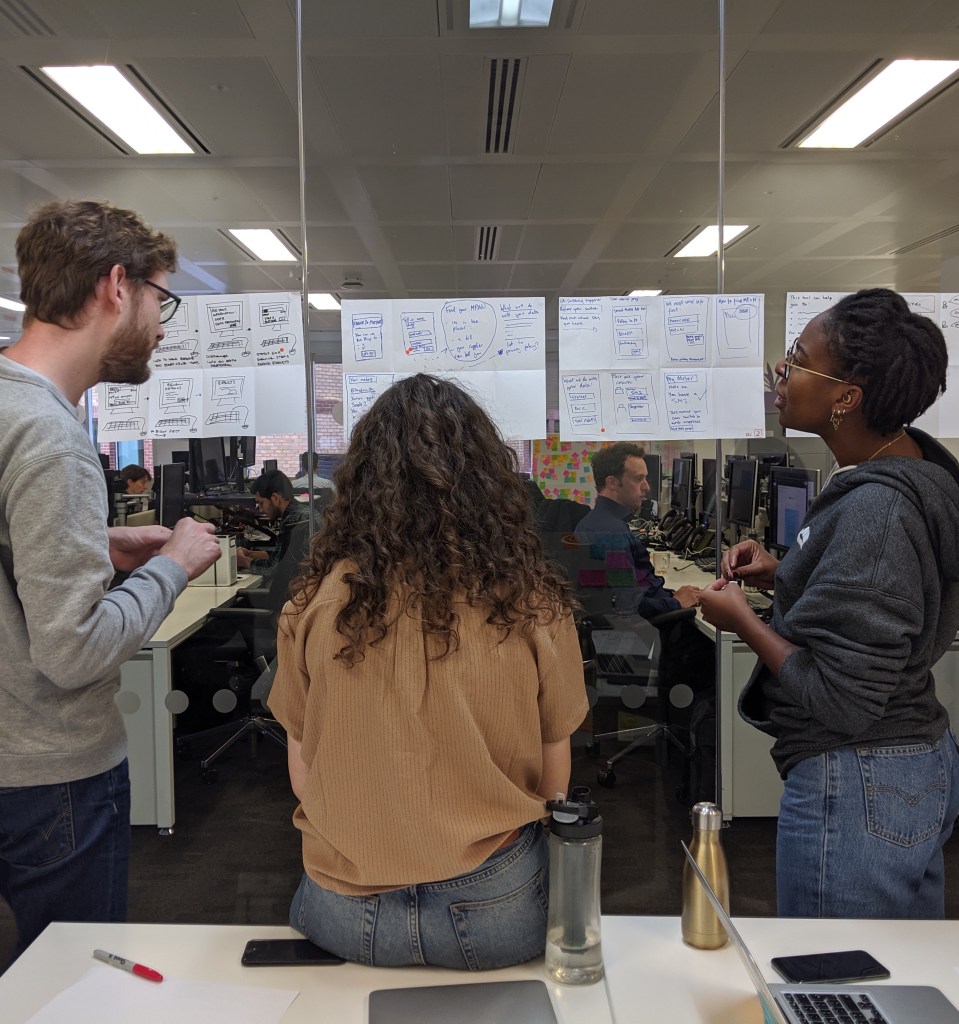 Design sprint team discuss ideas while looking at rapid UX sketches