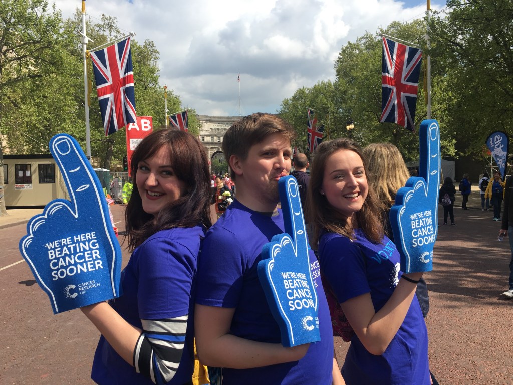 Becky and friends volunteering at the London Marathon wearing their Cancer Research UK t-shirts and waving branded foam fingers